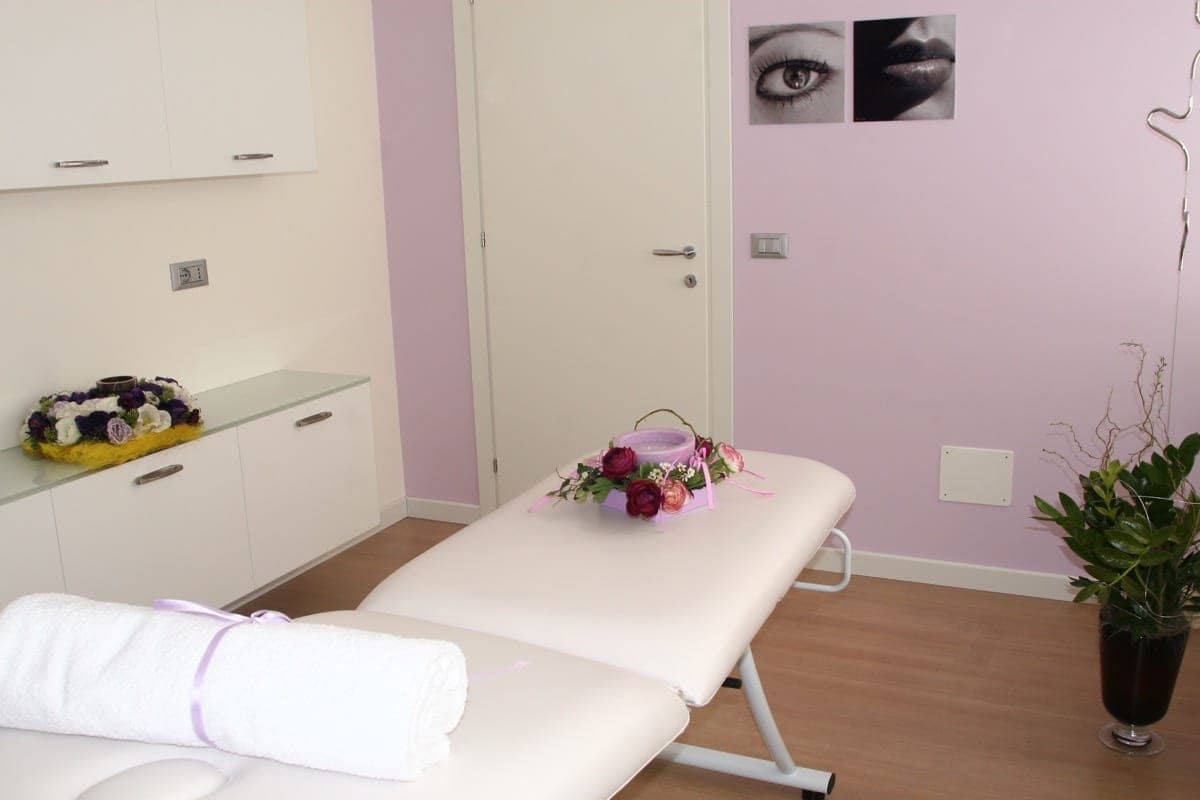 Cabina trattamenti con lettino bianco, asciugamano arrotolato e dettagli floreali