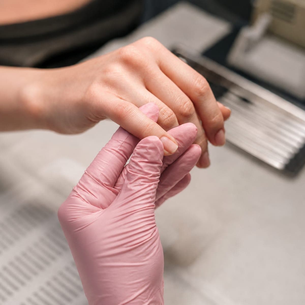 Mani durante una manicure professionale, con guanto rosa e cura delle unghie